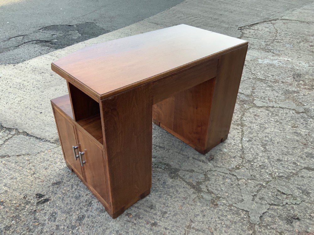 An Art Deco walnut desk featuring a left-hand pedestal of three drawers, a central kneehole drawer, an asymmetric stepped side tier, and metallic bar handles. View VI