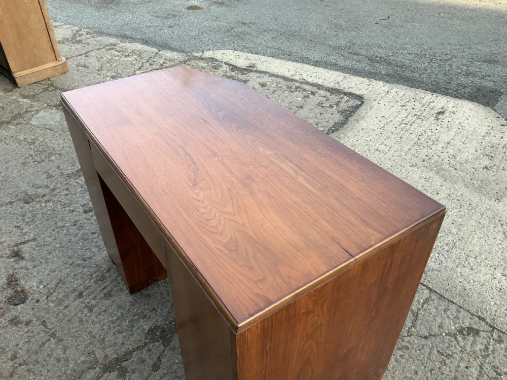 An Art Deco walnut desk featuring a left-hand pedestal of three drawers, a central kneehole drawer, an asymmetric stepped side tier, and metallic bar handles. View VII