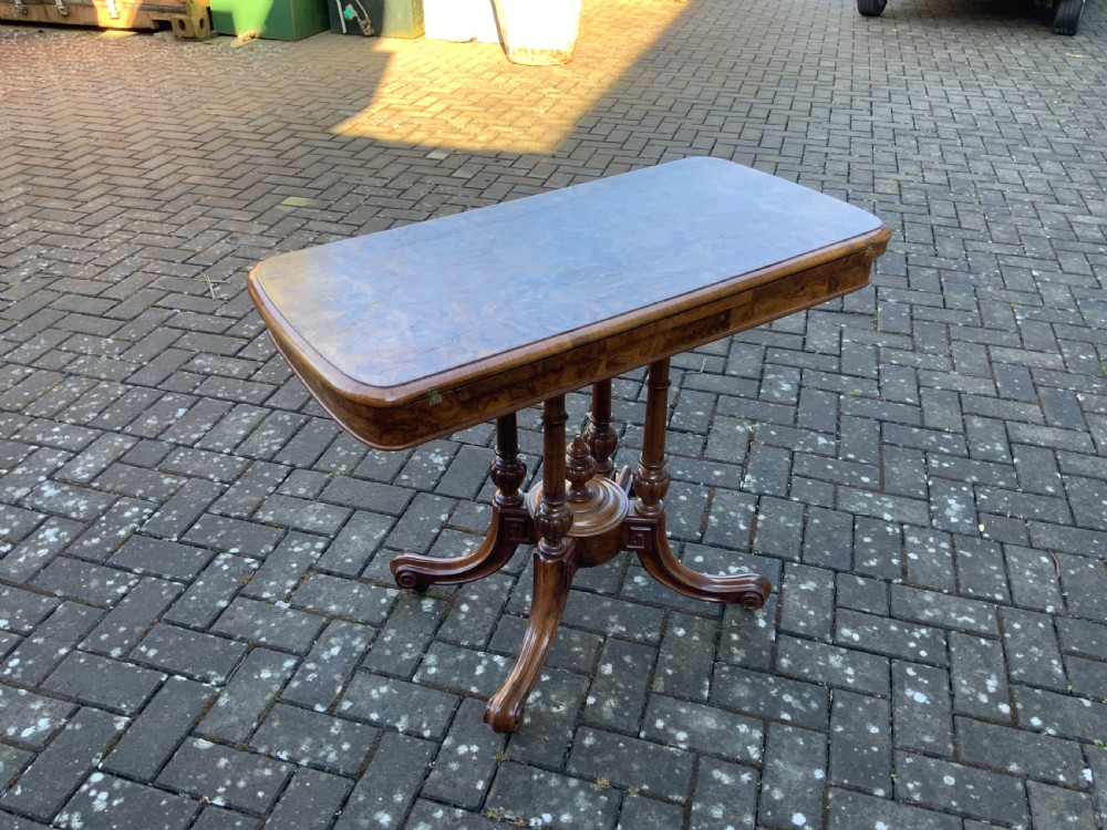 A Victorian burr walnut fold-top card table with highly figured wood grain, turned column supports, a central finial, and four carved splayed legs. View II