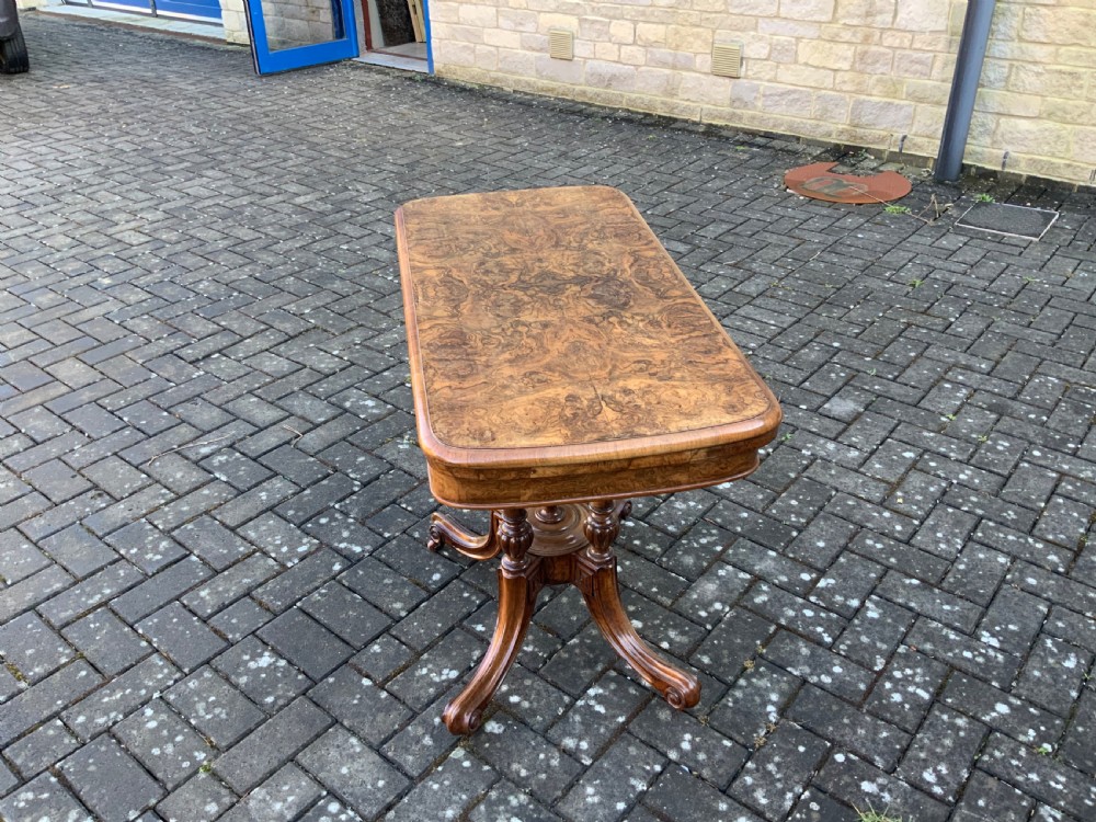 A Victorian burr walnut fold-top card table with highly figured wood grain, turned column supports, a central finial, and four carved splayed legs. View III