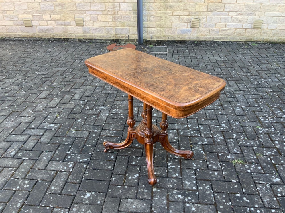 A Victorian burr walnut fold-top card table with highly figured wood grain, turned column supports, a central finial, and four carved splayed legs. View IV