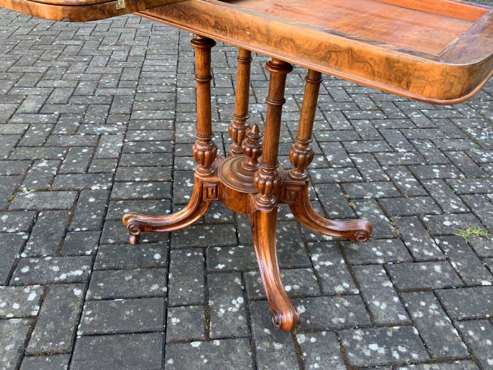 A Victorian burr walnut fold-top card table with highly figured wood grain, turned column supports, a central finial, and four carved splayed legs. View V