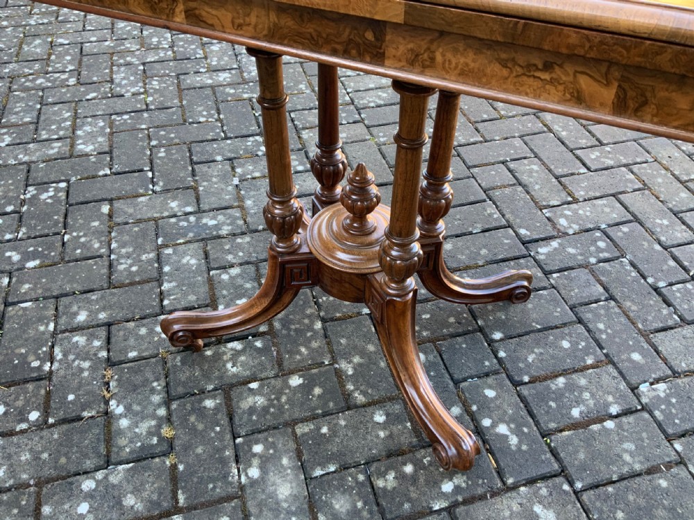 A Victorian burr walnut fold-top card table with highly figured wood grain, turned column supports, a central finial, and four carved splayed legs. View VI