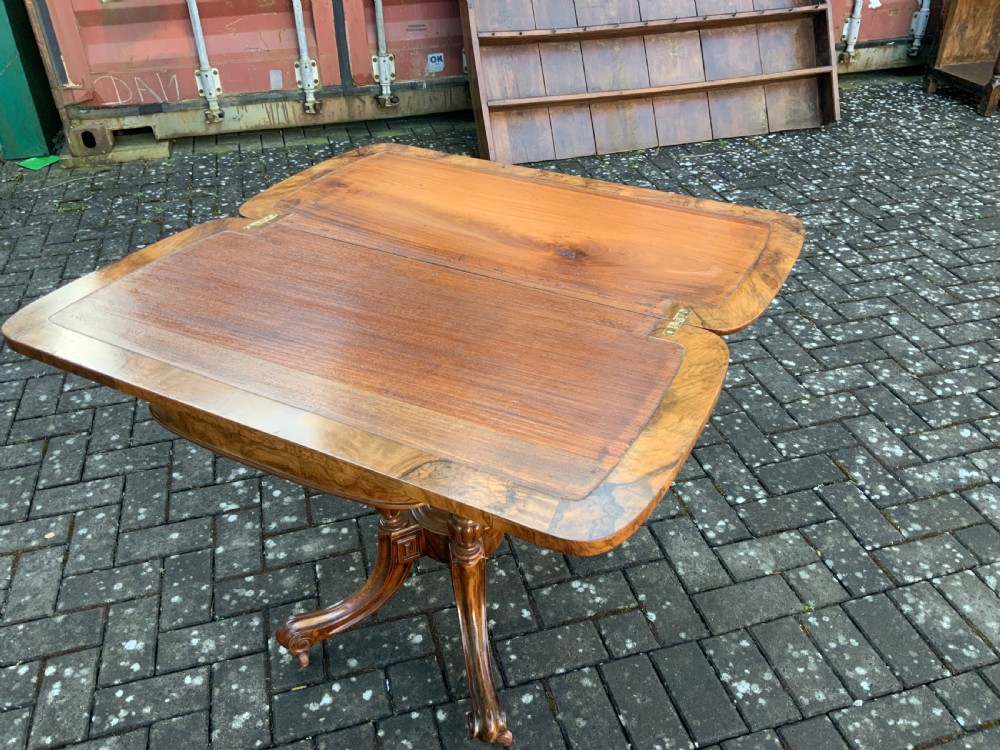 A Victorian burr walnut fold-top card table with highly figured wood grain, turned column supports, a central finial, and four carved splayed legs. View VIII