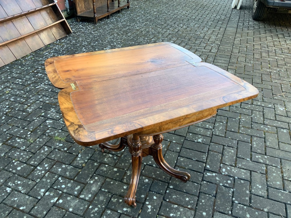 A Victorian burr walnut fold-top card table with highly figured wood grain, turned column supports, a central finial, and four carved splayed legs. View IX