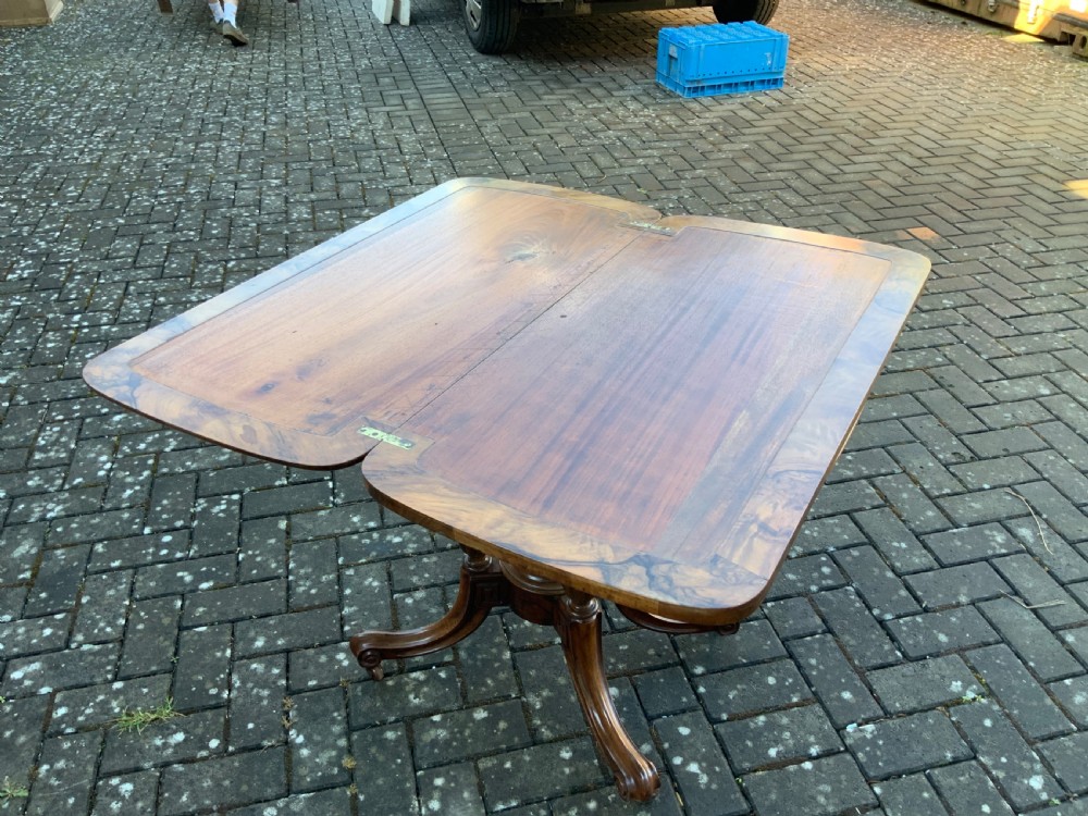 A Victorian burr walnut fold-top card table with highly figured wood grain, turned column supports, a central finial, and four carved splayed legs. View X
