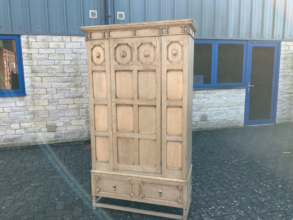 A light oak double wardrobe featuring geometric panelled doors, octagonal raised bosses, two base drawers, and turned legs. View III