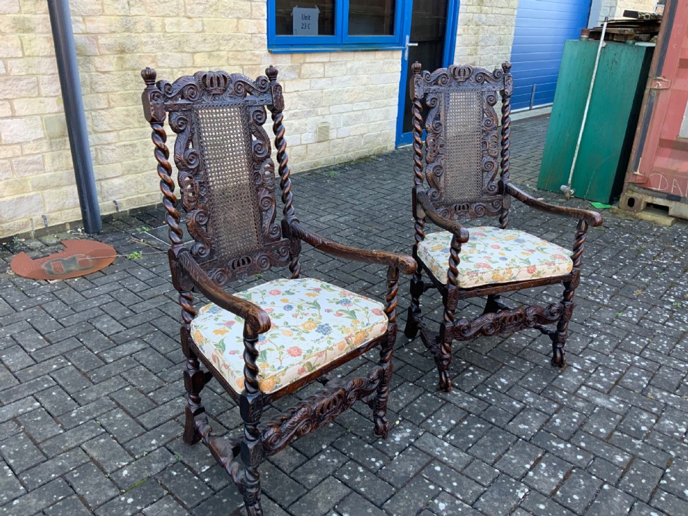 A pair of dark carved oak armchairs featuring high cane backs with carved crown crests, barley twist uprights, curved armrests, and floral upholstered seats. View II