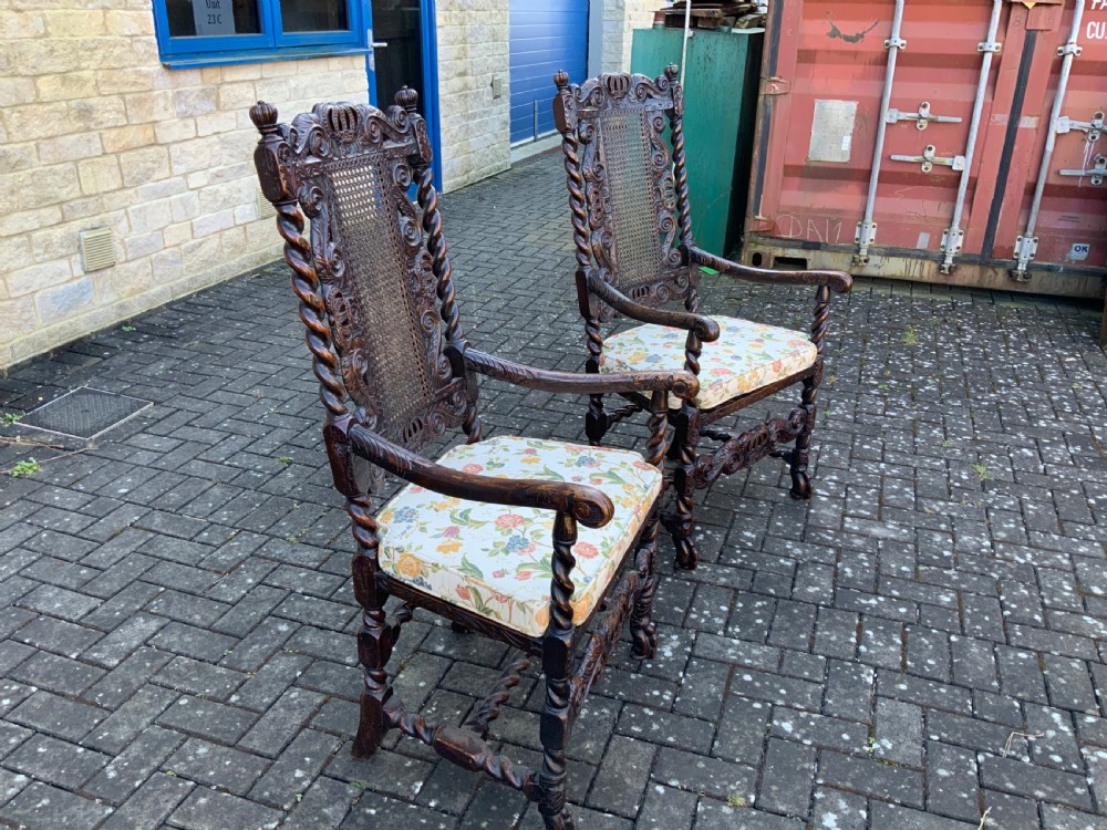 A pair of dark carved oak armchairs featuring high cane backs with carved crown crests, barley twist uprights, curved armrests, and floral upholstered seats. View III