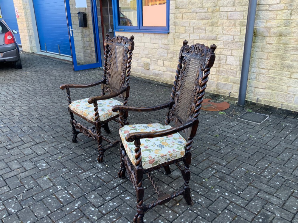 A pair of dark carved oak armchairs featuring high cane backs with carved crown crests, barley twist uprights, curved armrests, and floral upholstered seats. View IV