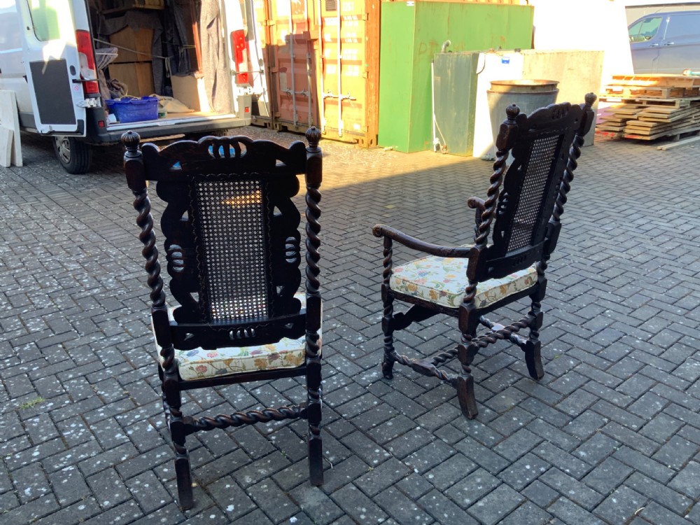 A pair of dark carved oak armchairs featuring high cane backs with carved crown crests, barley twist uprights, curved armrests, and floral upholstered seats. View VII