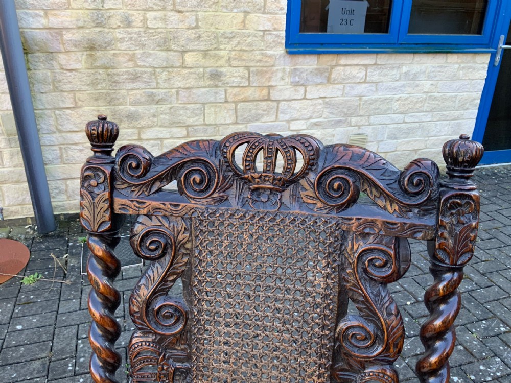 A pair of dark carved oak armchairs featuring high cane backs with carved crown crests, barley twist uprights, curved armrests, and floral upholstered seats. View VIII