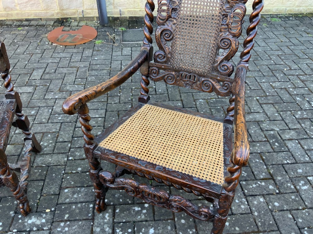 A pair of dark carved oak armchairs featuring high cane backs with carved crown crests, barley twist uprights, curved armrests, and floral upholstered seats. View IX