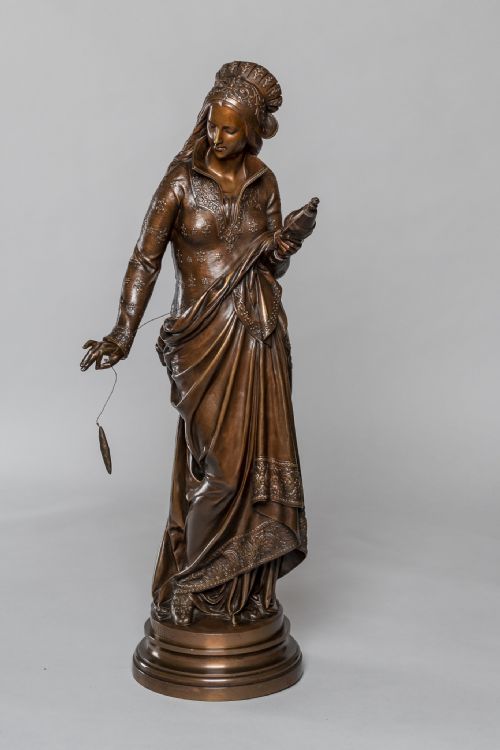 fig 1. A 19th-century dark patinated bronze sculpture depicting a woman in detailed historical attire holding a distaff and thread, standing on a circular moulded base.
