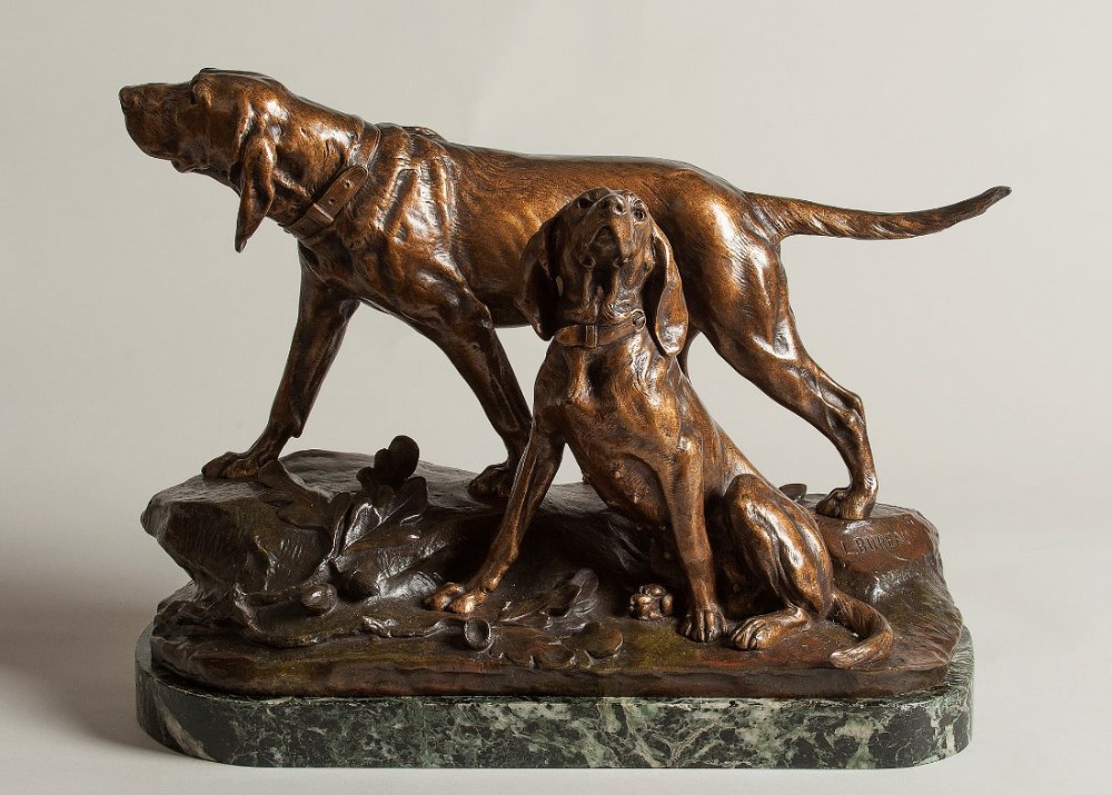 A French bronze sculpture depicting two alert hunting hounds standing and sitting on a rocky terrain base mounted on a green marble plinth.