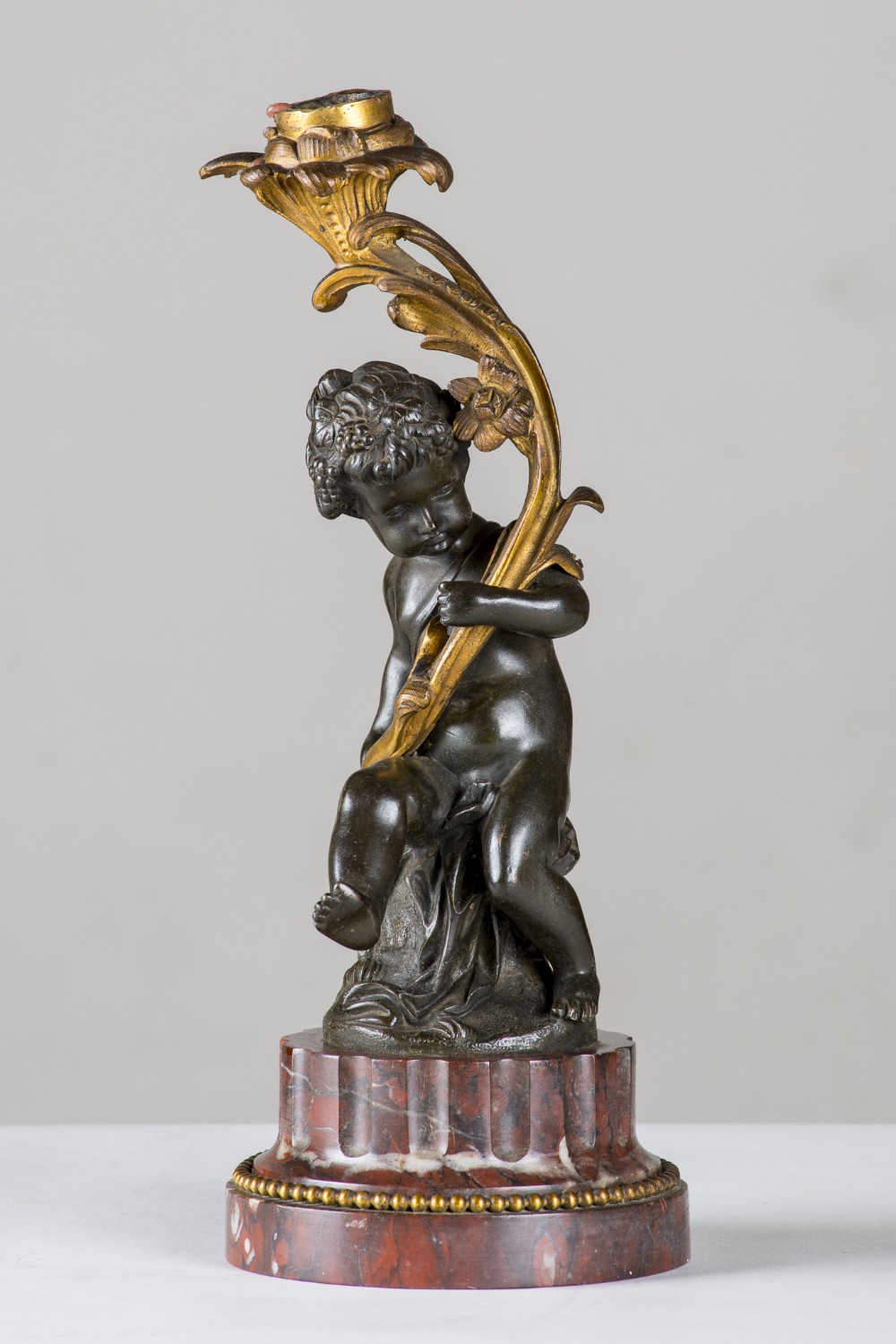 A 19th-century French patinated bronze figure of a cherub holding a gilt bronze floral candlestick stem, mounted on a fluted red marble base.