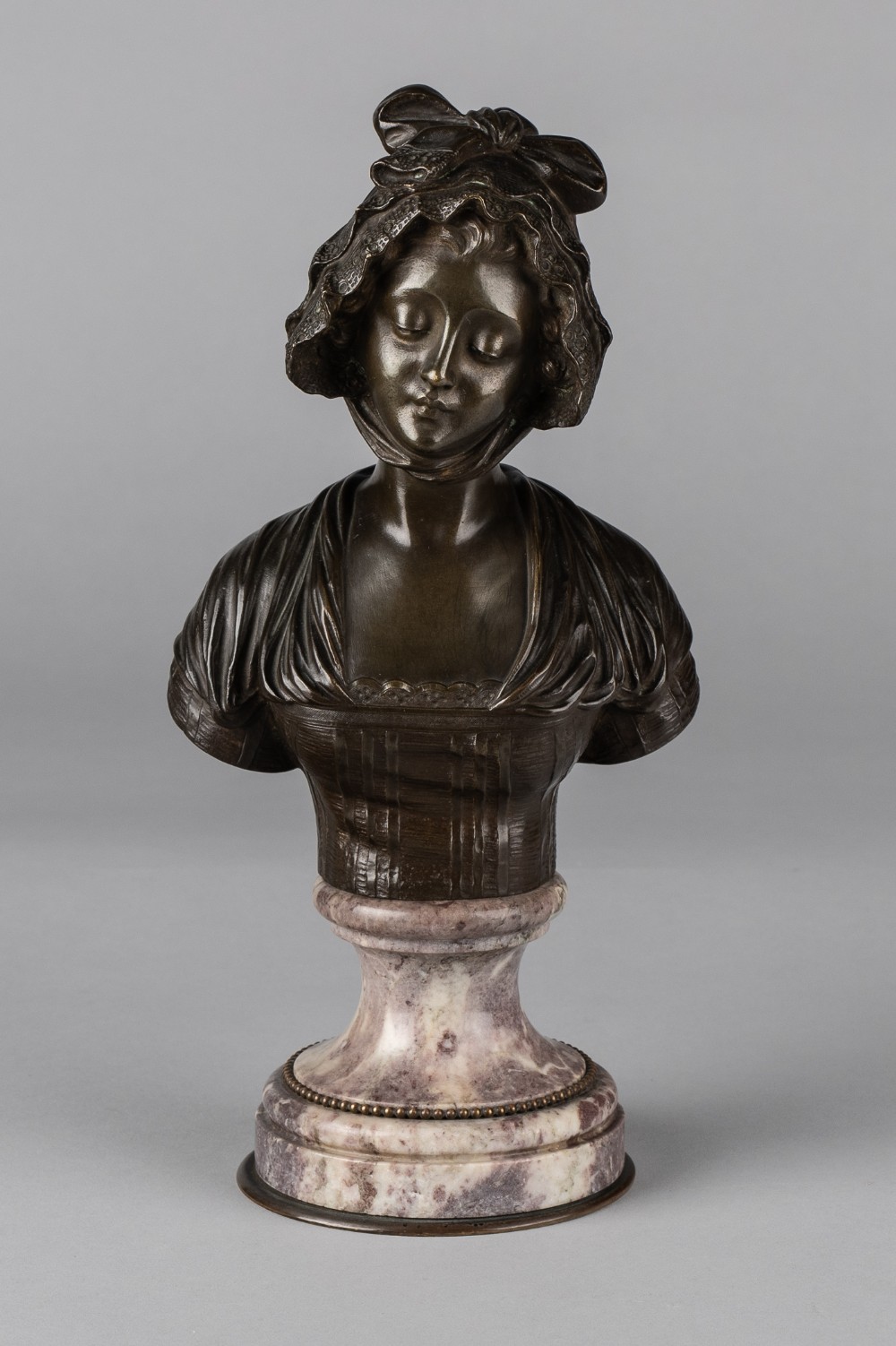 A nineteenth-century French bronze bust of a woman wearing a lace bonnet, set on a turned variegated marble socle.