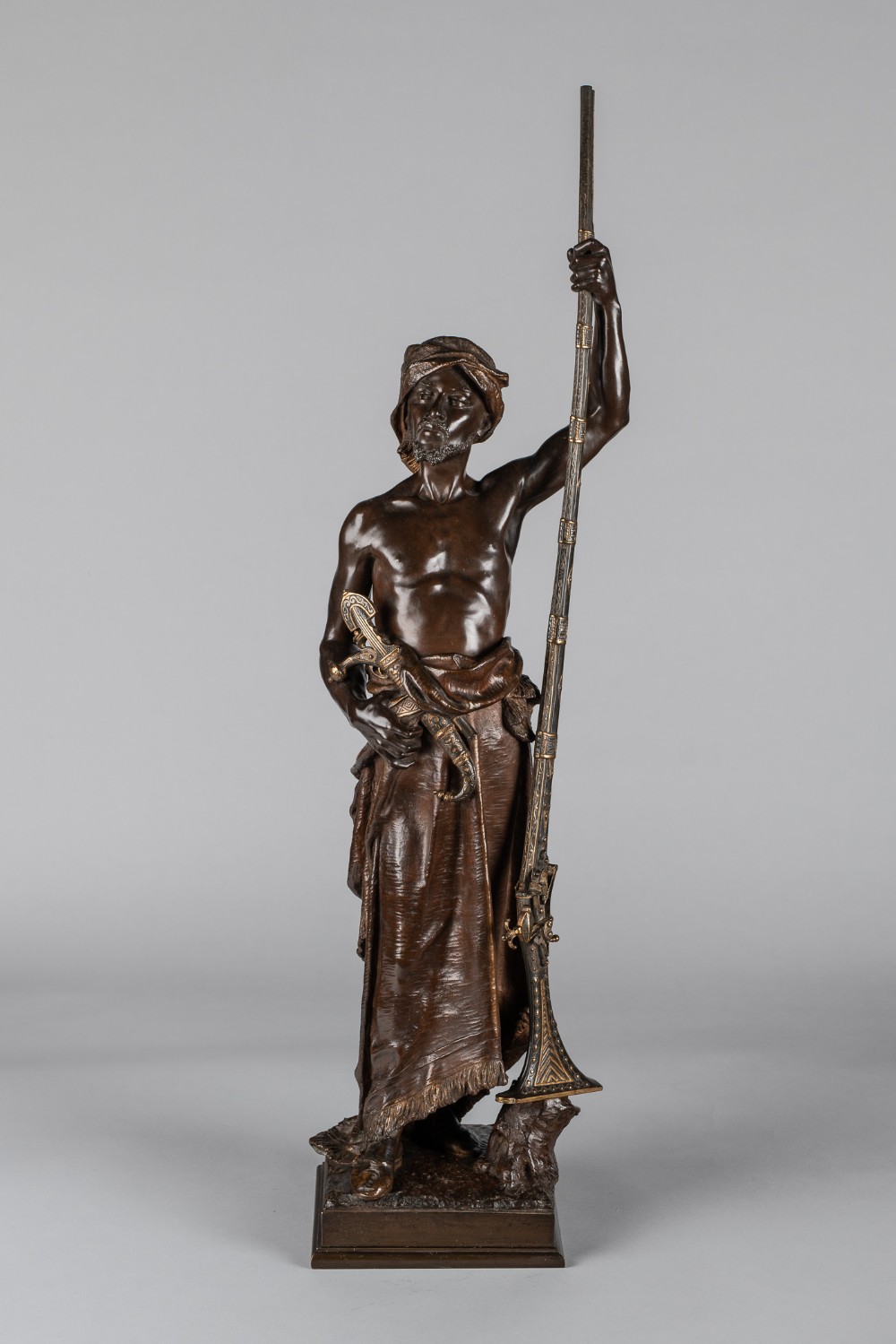 A 19th-century dark patinated bronze sculpture depicting an Arabian sentinel holding a long rifle upright with a dagger tucked into his waistband.