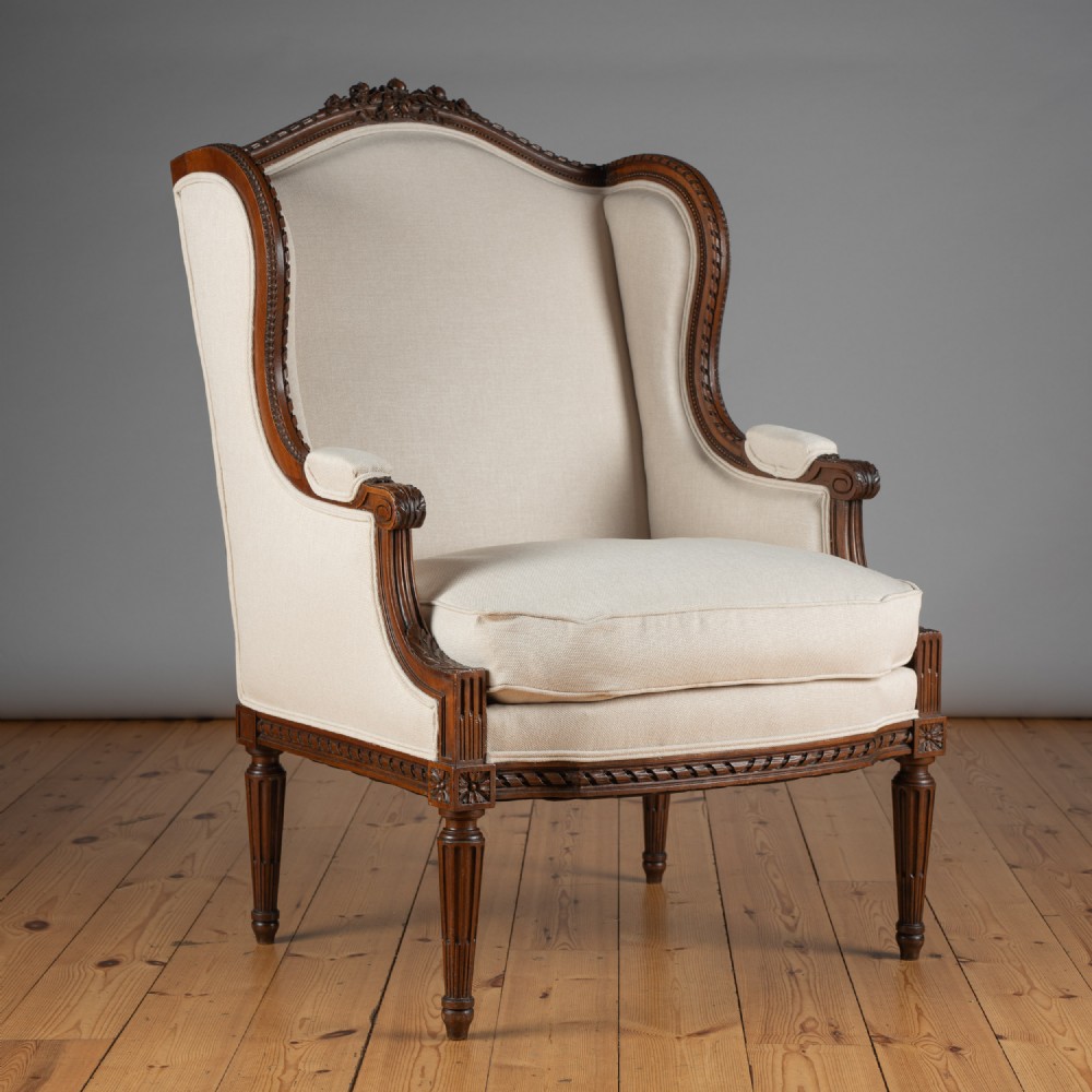 A 19th-century French carved walnut bergere armchair with cream linen upholstery and fluted legs.