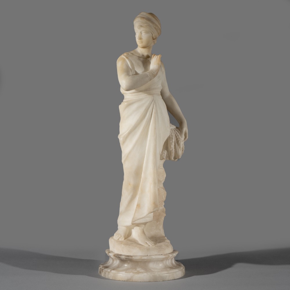 A full-length carved off-white alabaster sculpture depicting a draped female figure standing on a rounded moulded pedestal.