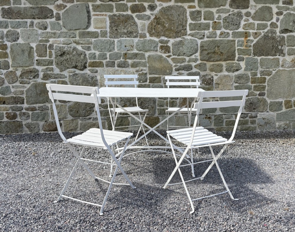 A white painted French iron and wooden slatted folding bistro table with four matching folding chairs.