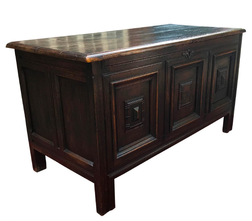 A dark oak 17th-century coffer with a rectangular hinged lid and three geometric panelled sections on the front facade.