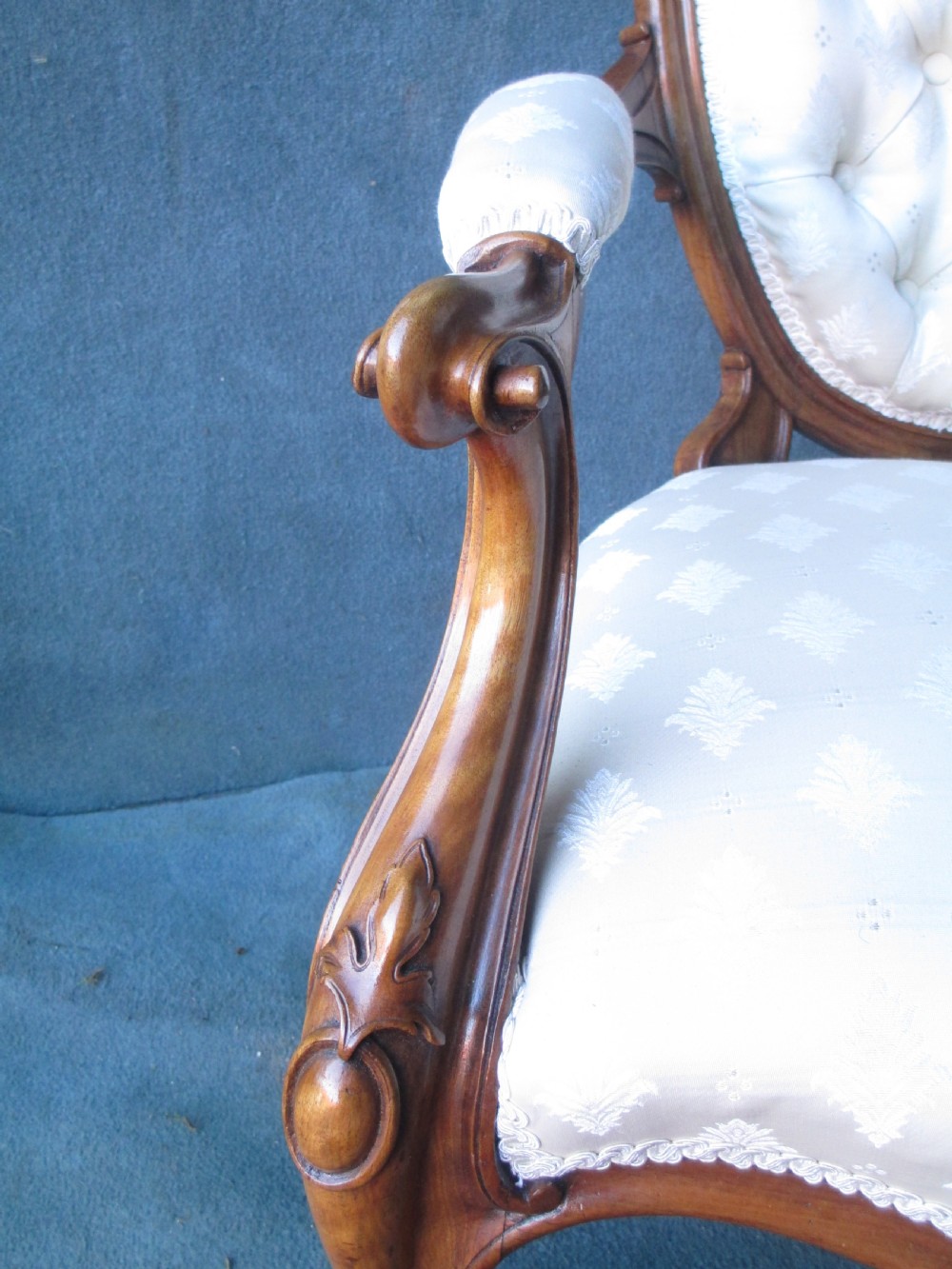 An antique Victorian walnut armchair featuring an oval buttoned backrest, cream patterned fabric upholstery, padded armrests, and carved cabriole legs. View II