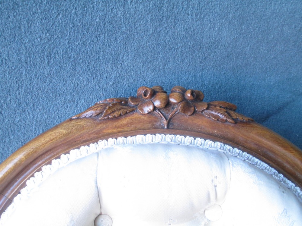 An antique Victorian walnut armchair featuring an oval buttoned backrest, cream patterned fabric upholstery, padded armrests, and carved cabriole legs. View III