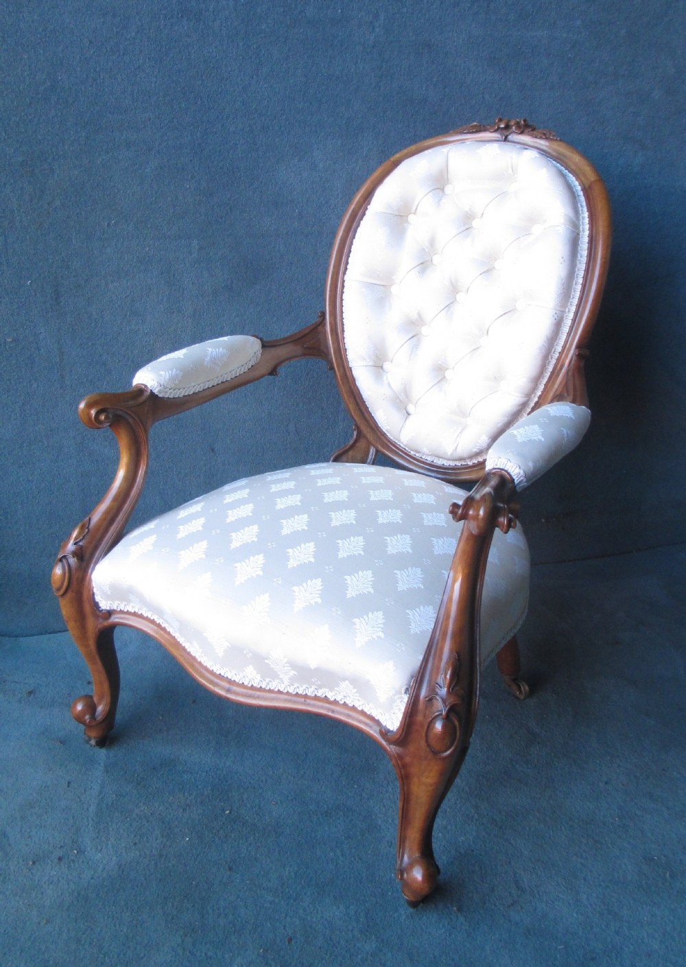 An antique Victorian walnut armchair featuring an oval buttoned backrest, cream patterned fabric upholstery, padded armrests, and carved cabriole legs. View IV