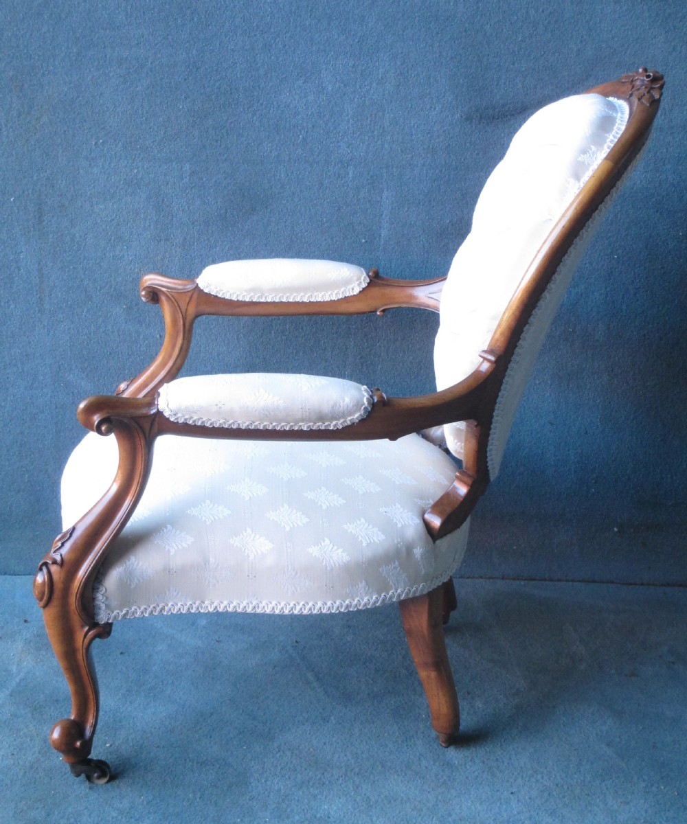 An antique Victorian walnut armchair featuring an oval buttoned backrest, cream patterned fabric upholstery, padded armrests, and carved cabriole legs. View V