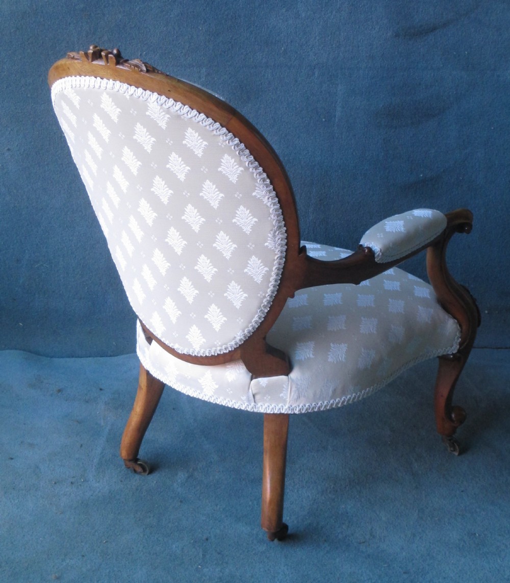 An antique Victorian walnut armchair featuring an oval buttoned backrest, cream patterned fabric upholstery, padded armrests, and carved cabriole legs. View VI