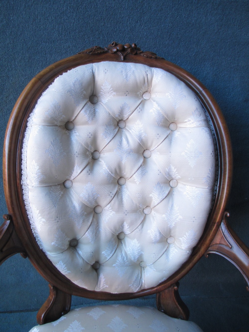 An antique Victorian walnut armchair featuring an oval buttoned backrest, cream patterned fabric upholstery, padded armrests, and carved cabriole legs. View VII