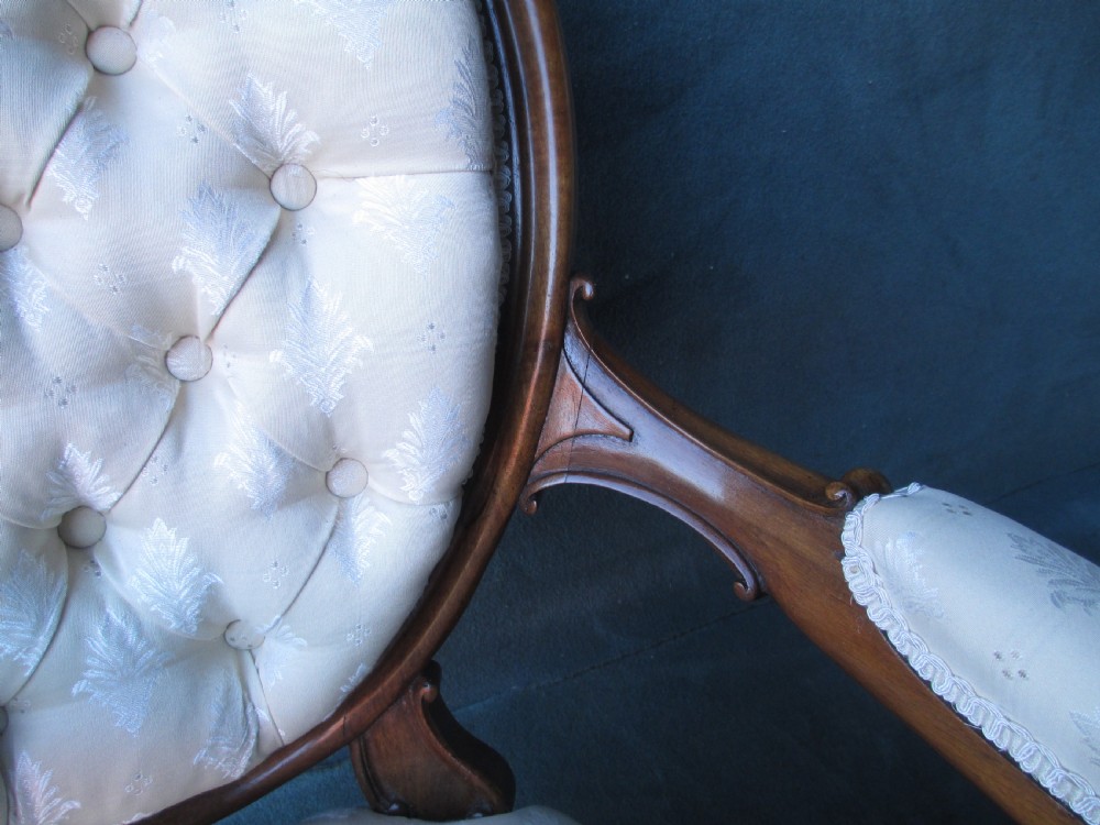 An antique Victorian walnut armchair featuring an oval buttoned backrest, cream patterned fabric upholstery, padded armrests, and carved cabriole legs. View VIII