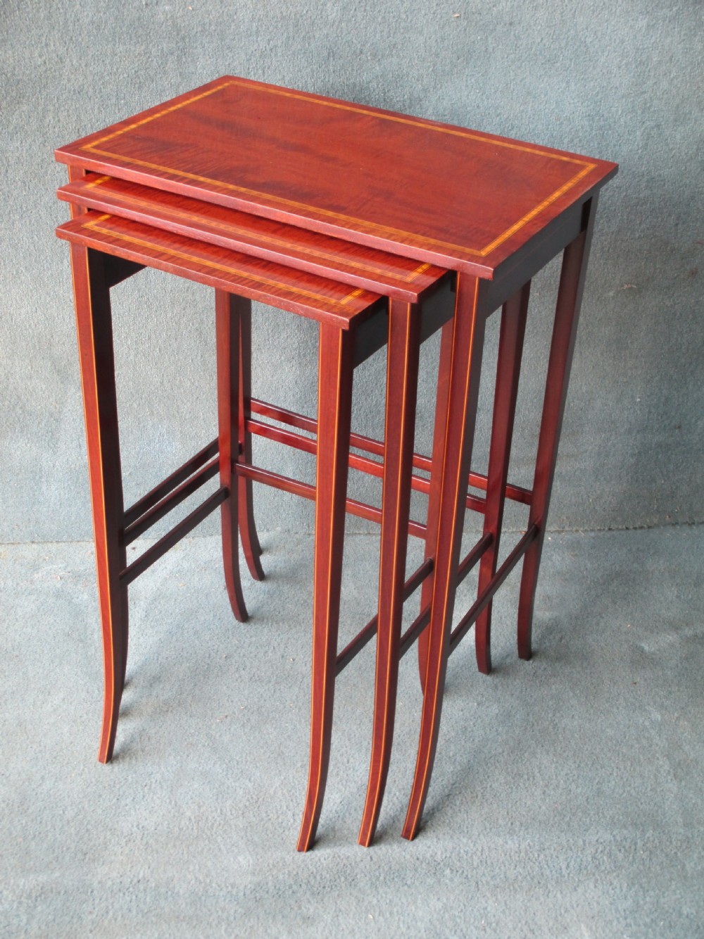 A set of three graduated mahogany nesting tables featuring satinwood stringing inlay along the tops and slender, slightly splayed legs.