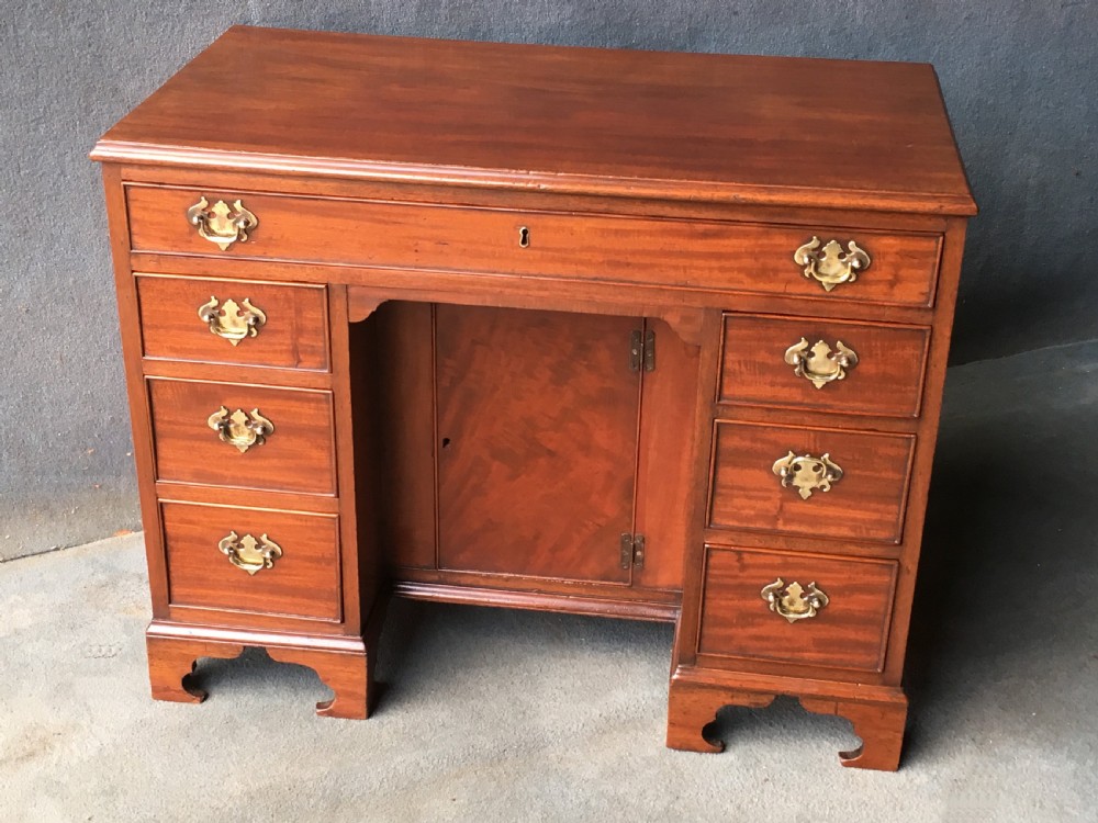 A Georgian style mahogany kneehole desk featuring a flat top, seven pedestal drawers with brass handles, a central recessed cupboard, and bracket feet.