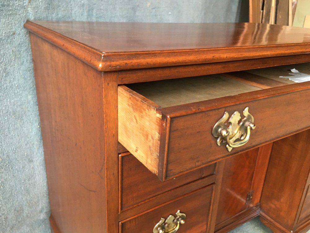 A Georgian style mahogany kneehole desk featuring a flat top, seven pedestal drawers with brass handles, a central recessed cupboard, and bracket feet. View III