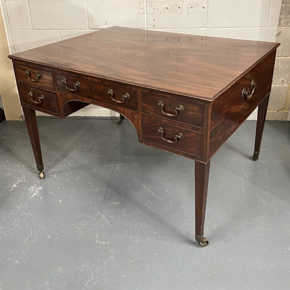A Georgian mahogany partners writing table featuring multiple drawers with brass drop handles, side carrying handles, and tapered legs on brass castors.