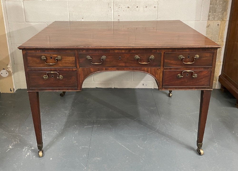 A Georgian mahogany partners writing table featuring multiple drawers with brass drop handles, side carrying handles, and tapered legs on brass castors. View II