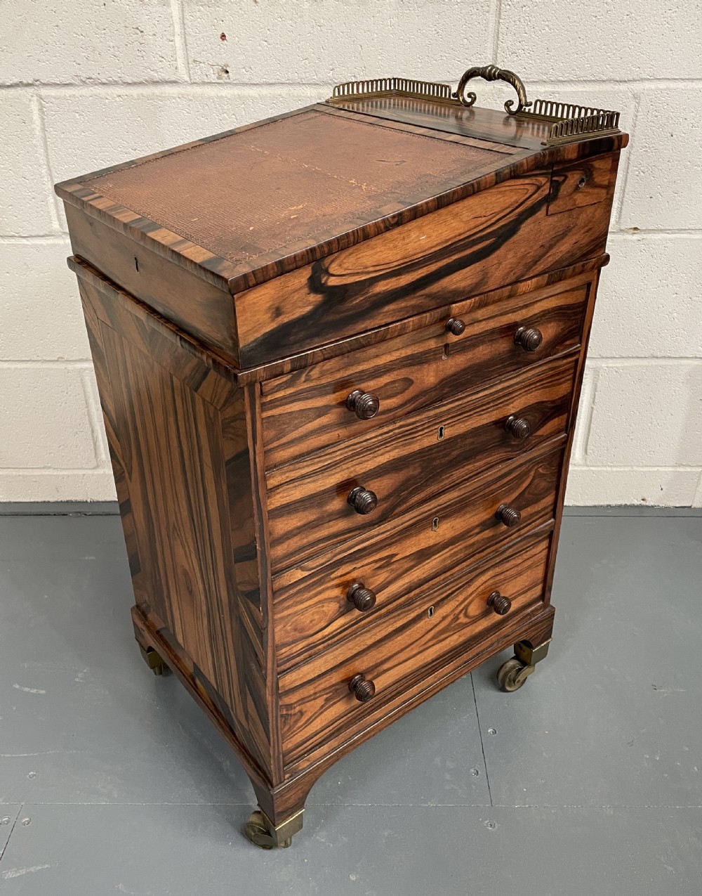 A Regency period coromandel Davenport desk featuring a slanted leather inset writing top, top brass gallery, turned wood knobs, and side drawers on brass castors.