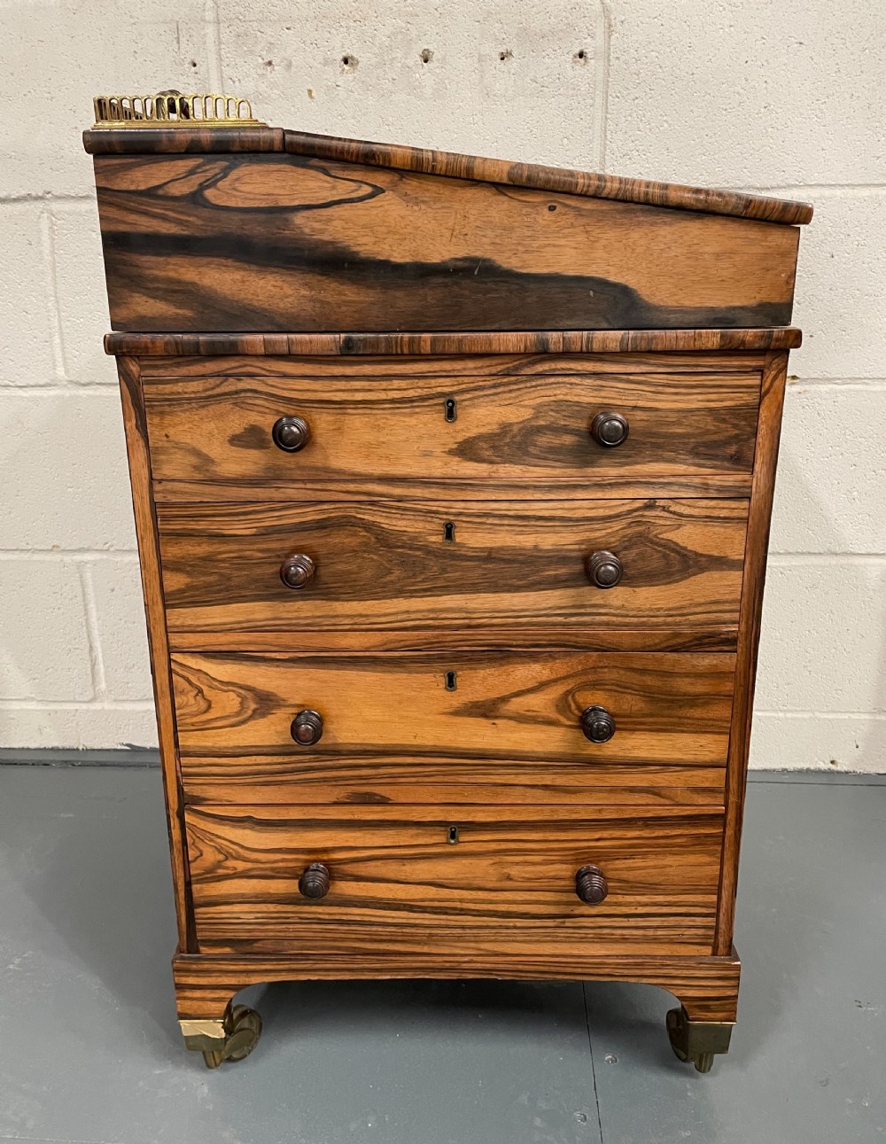 A Regency period coromandel Davenport desk featuring a slanted leather inset writing top, top brass gallery, turned wood knobs, and side drawers on brass castors. View III