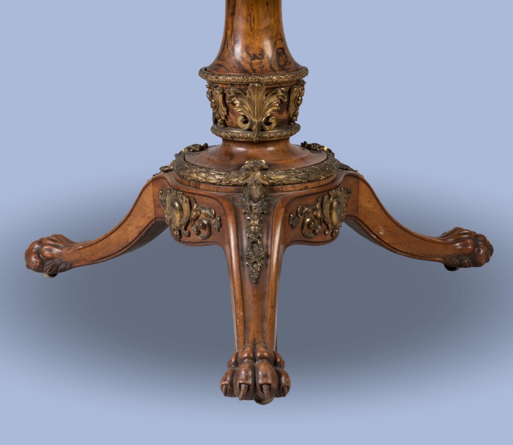 A circular Victorian burr walnut centre table featuring inlaid marquetry cartouches along the border and a carved pedestal base. View II