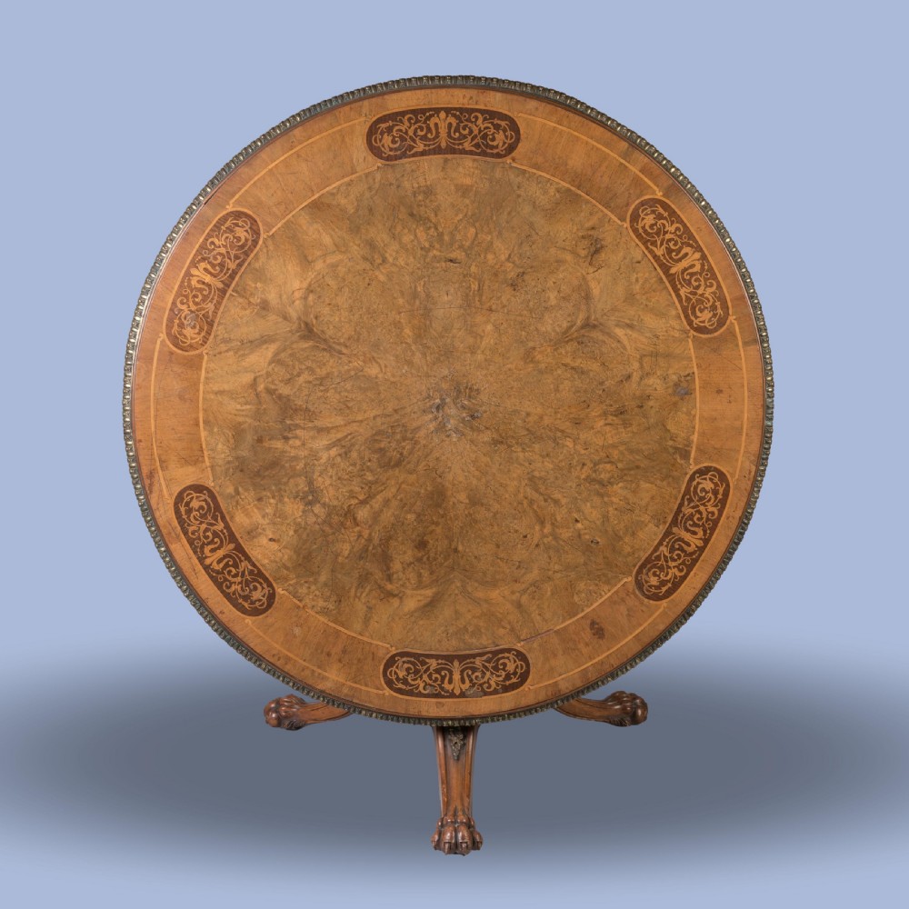 A circular Victorian burr walnut centre table featuring inlaid marquetry cartouches along the border and a carved pedestal base. View III