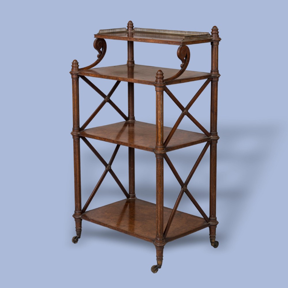 An antique walnut tiered whatnot with X-frame sides, turned columns, brass castors, and a small top shelf with a brass gallery rail.