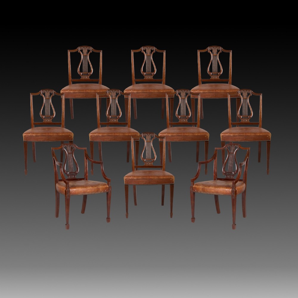 A set of ten carved mahogany dining chairs featuring lyre backs, brown leather upholstered seats with stud trim, and fluted legs.