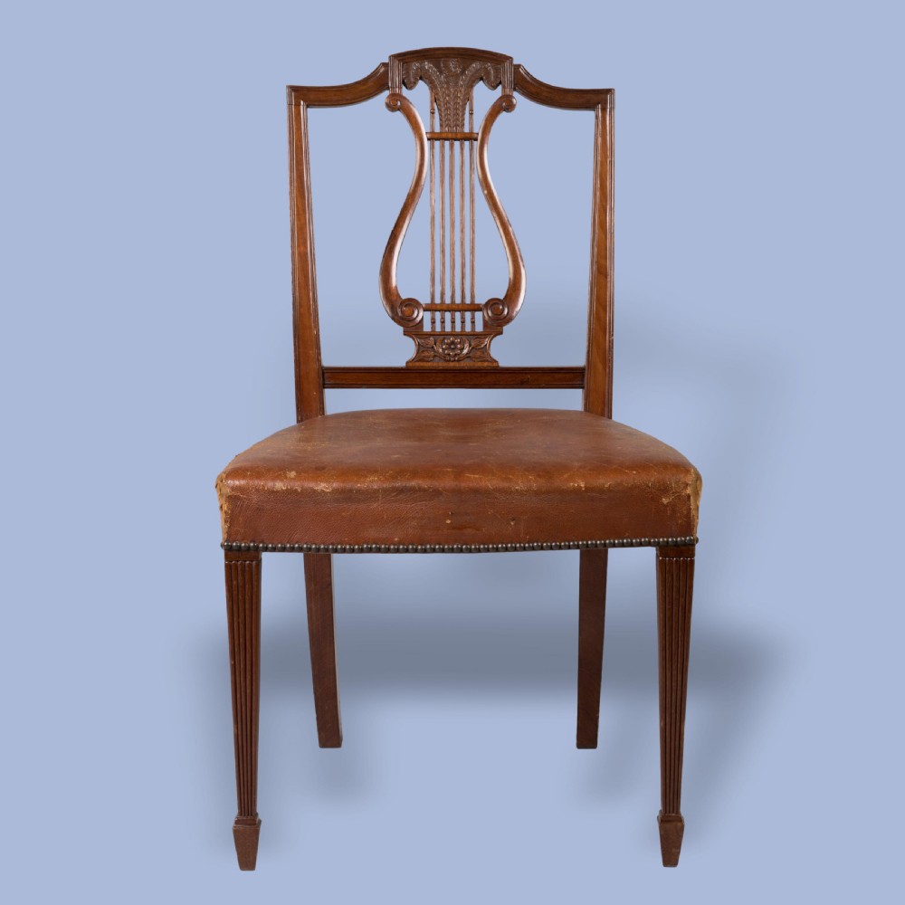 A set of ten carved mahogany dining chairs featuring lyre backs, brown leather upholstered seats with stud trim, and fluted legs. View V