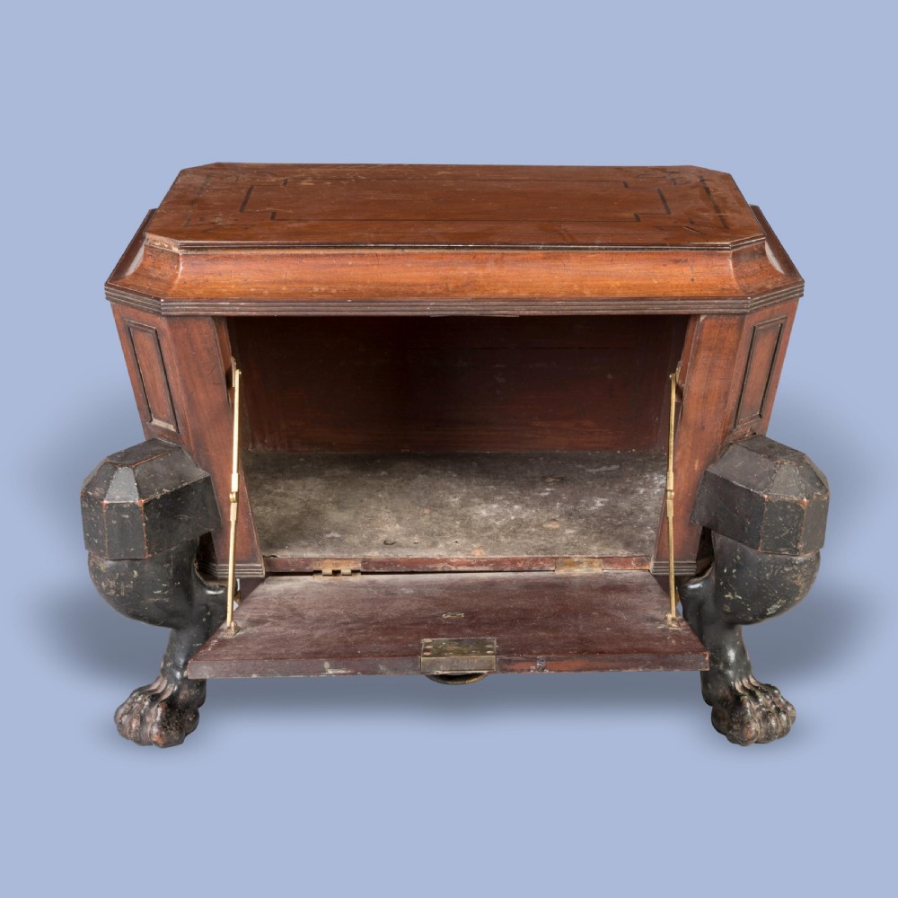 A Regency mahogany sarcophagus-form wine cellarette featuring Greek key inlay, a central brass lion-mask ring handle, and ebonised monopodia lion paw legs. View III