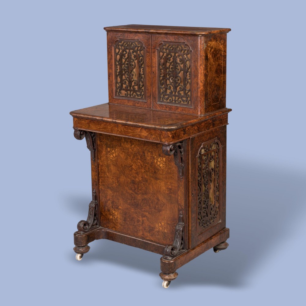A mid-nineteenth-century Victorian burr walnut Davenport desk featuring pierced fretwork cabinet doors, floral marquetry inlay, carved scroll brackets, and ceramic castors.