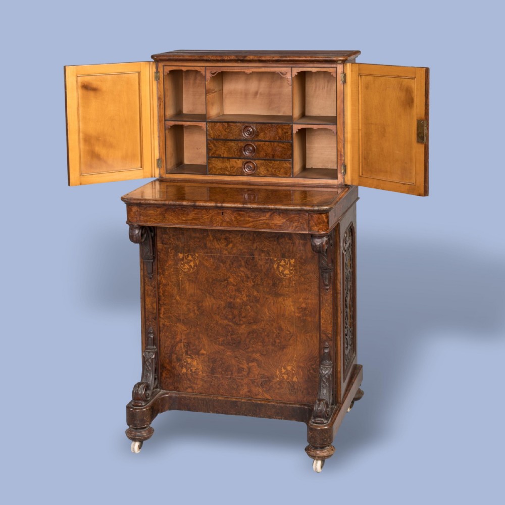 A mid-nineteenth-century Victorian burr walnut Davenport desk featuring pierced fretwork cabinet doors, floral marquetry inlay, carved scroll brackets, and ceramic castors. View IV