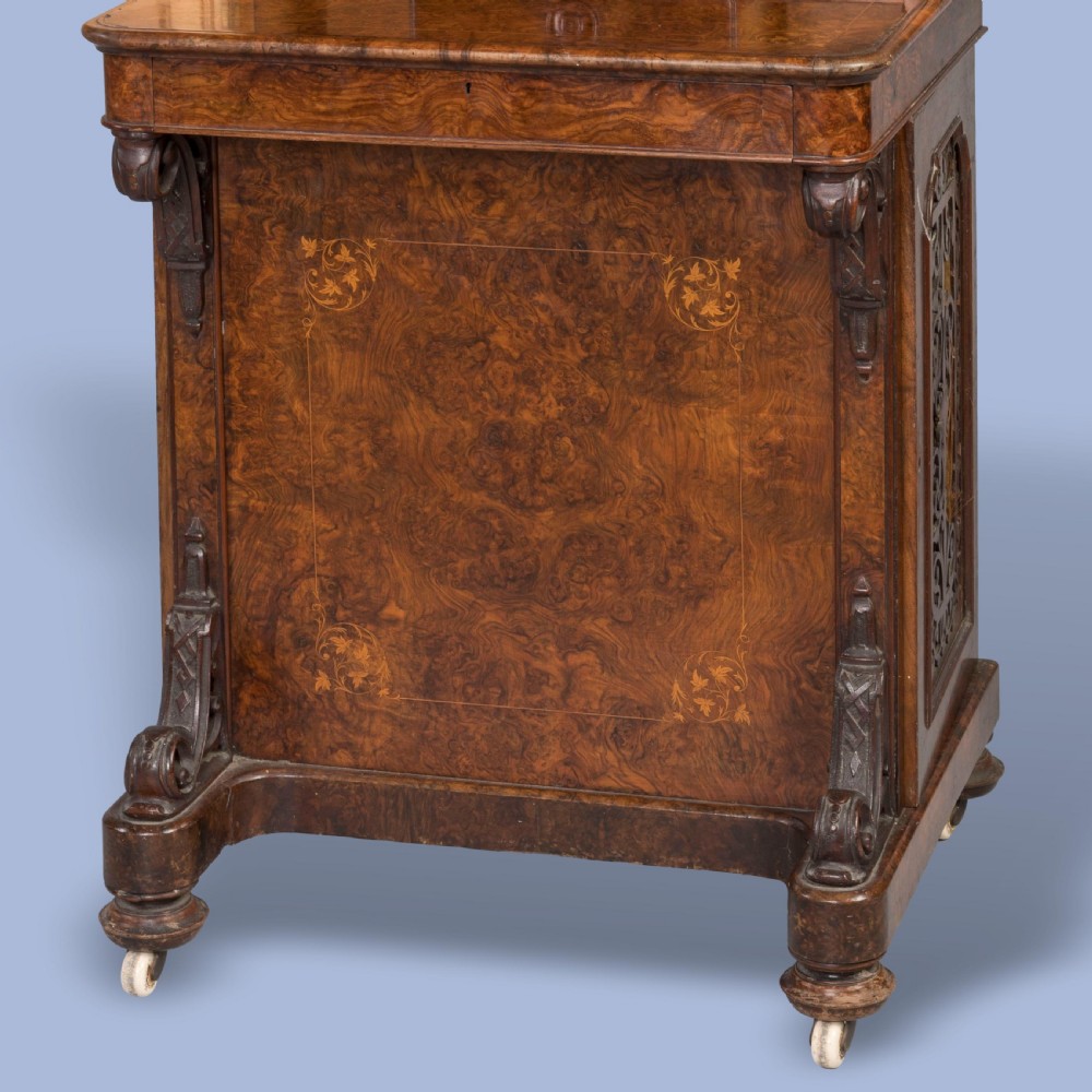 A mid-nineteenth-century Victorian burr walnut Davenport desk featuring pierced fretwork cabinet doors, floral marquetry inlay, carved scroll brackets, and ceramic castors. View V