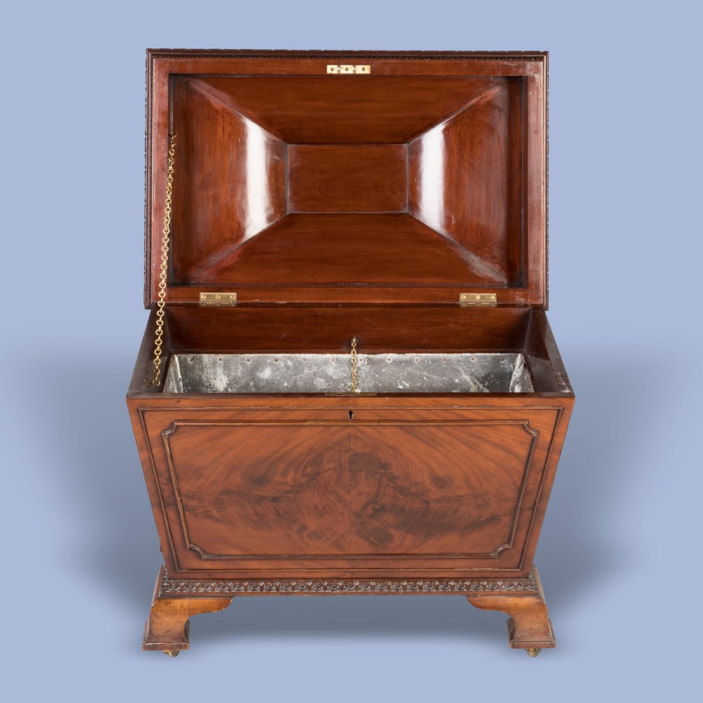 A sarcophagus-shaped antique mahogany wine cooler with carved decorative borders, side brass carrying handles, and brass castors. View III